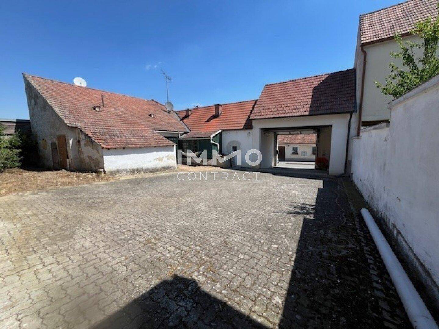 Gepflasterter Innenhof mit mehreren Gebäuden und einer Durchfahrt, ideal für Parkplätze.