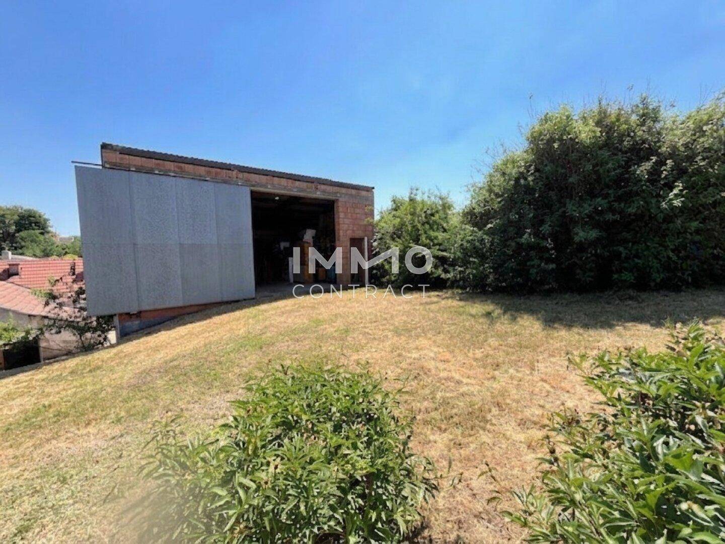Gartenbereich mit trockenem Rasen und einem Ziegelgebäude im Hintergrund unter blauem Himmel.