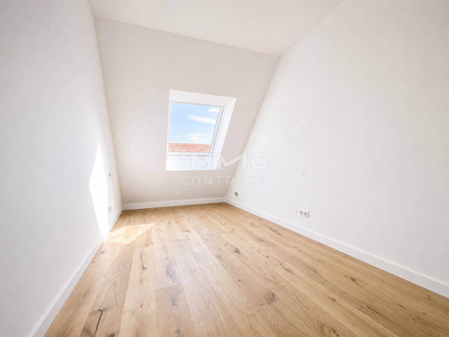 Heller Dachraum mit schrägem Dach und einem Fenster, das einen Blick nach draußen bietet.
