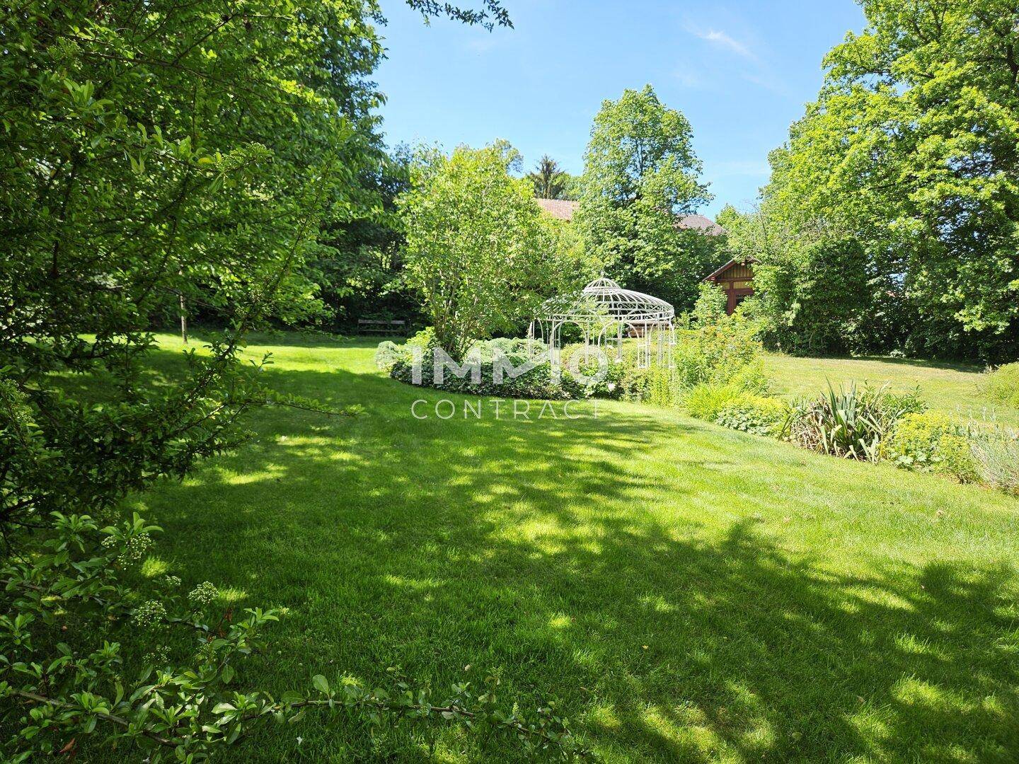 Idyllischer, weitläufiger Garten mit gepflegtem Rasen, altem Baumbestand und einem dekorativen Pavillon.