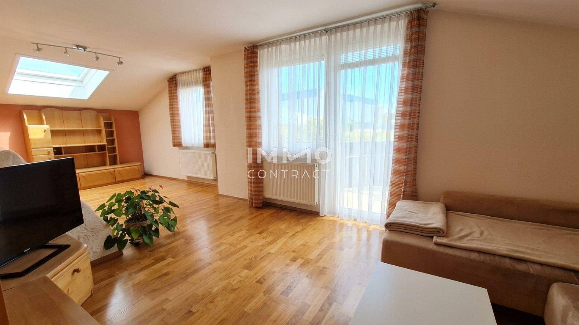 Helles Wohnzimmer mit Holzboden, Dachfenster und Zugang zu einem Außenbereich.