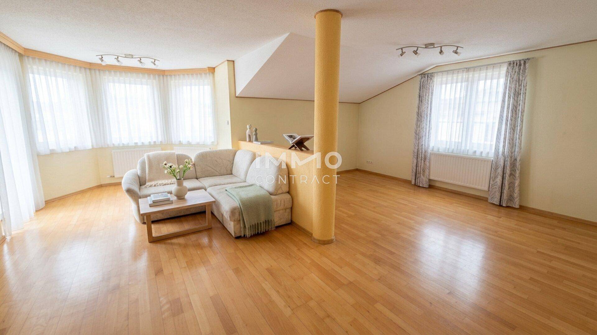 Geräumiges Wohnzimmer mit Holzboden, großer Couch und vielen Fenstern für viel Tageslicht.