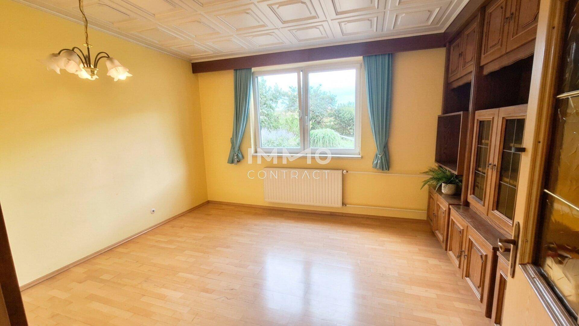 Geräumiges Wohnzimmer mit Holzboden, großem Fenster und traditionellen Möbeln sowie einer Zierdecke.