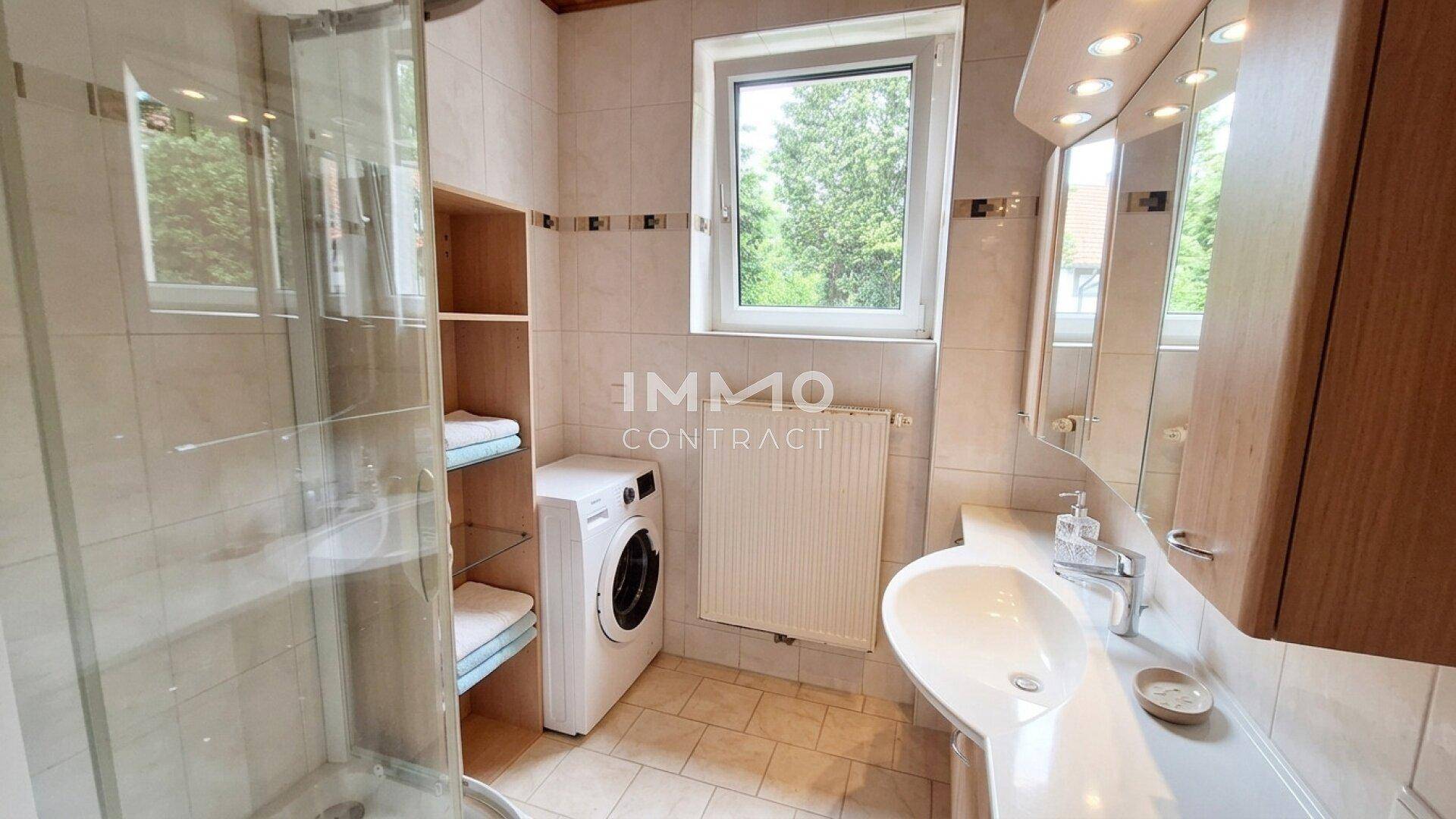 Badezimmer mit Dusche, Waschbecken, Waschmaschine und Fenster für natürliche Belüftung.