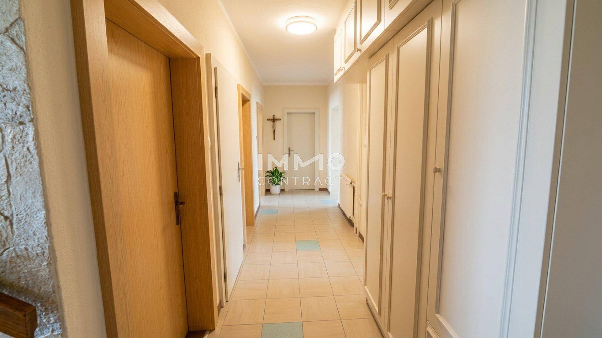 Langer Flur mit Einbauschränken, Fliesenboden und Holztüren, der zu weiteren Räumen führt.