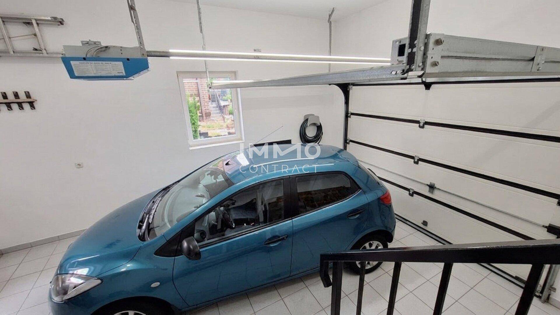 Garage mit automatischem Tor, Fenster und Platz für ein Fahrzeug, gut beleuchtet.