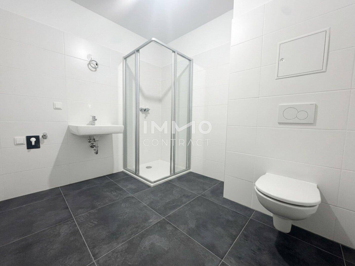 Modernes Badezimmer mit weißen Wandfliesen, dunklem Boden, Duschkabine und wandhängendem WC.