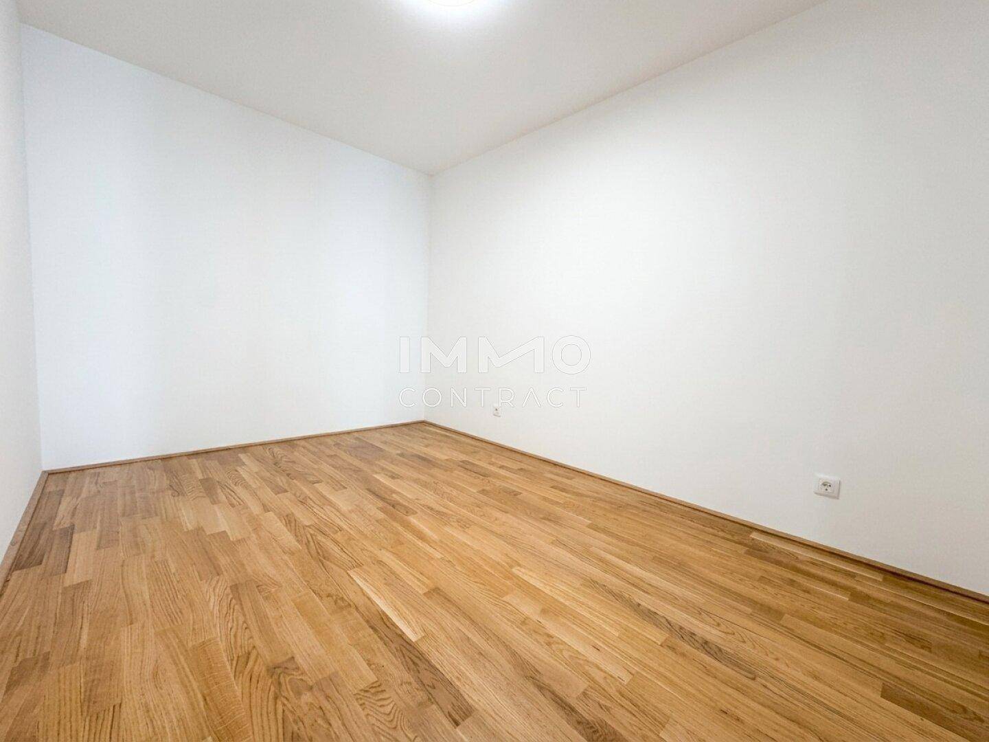 Schlichter, leerer Raum mit hellem Parkettboden und weißen Wänden, ideal als Schlaf- oder Arbeitszimmer.