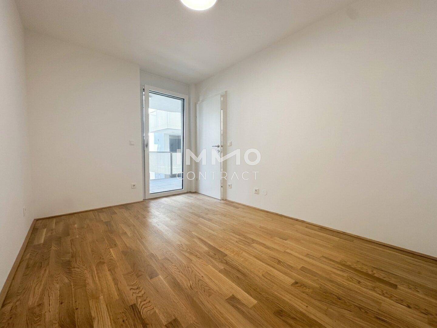 Leeres Schlafzimmer mit Parkettboden und direktem Zugang zu einem Balkon oder einer Terrasse.