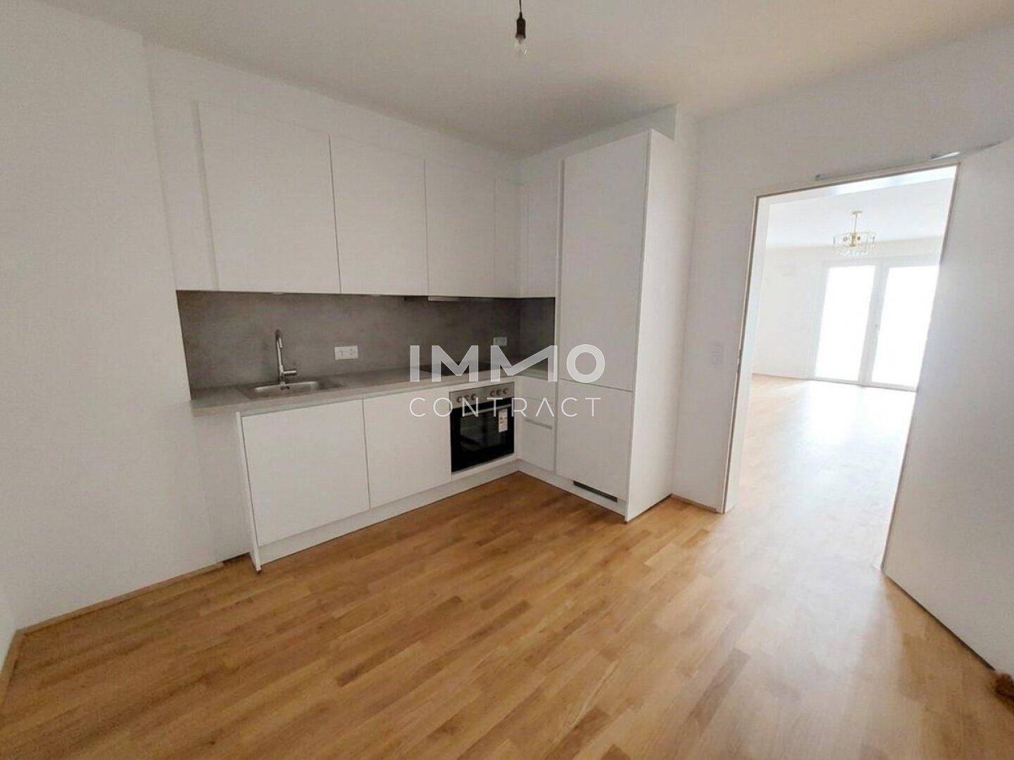 Kompakte, moderne Küche mit weißen Schränken, integriertem Backofen und Holzboden.