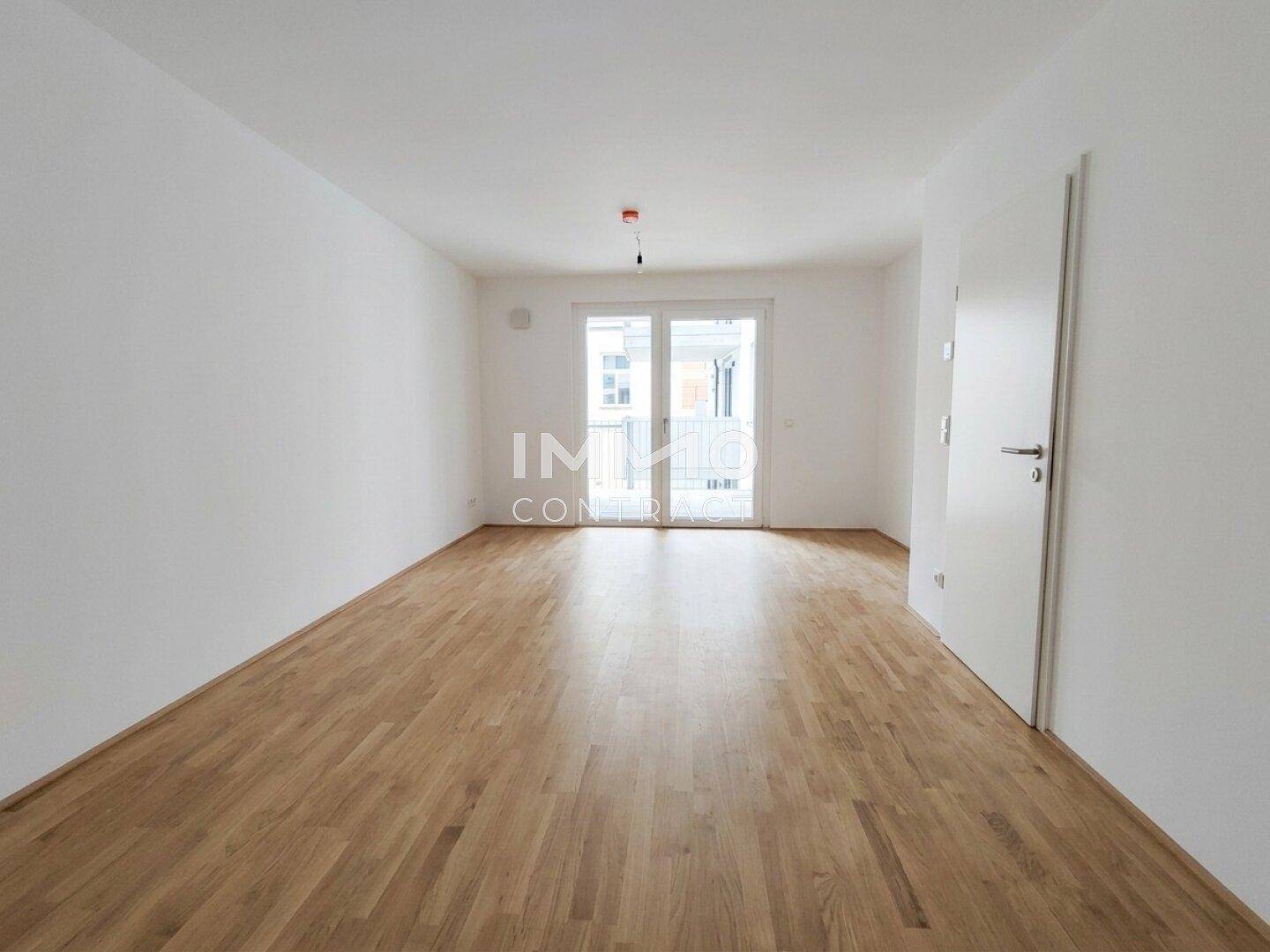 Heller, leerer Raum mit Holzboden und Zugang zu einem Balkon oder einer Terrasse.