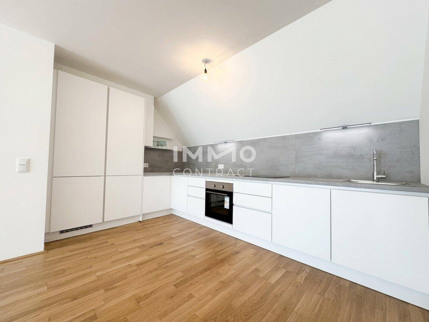 Moderne weiße Einbauküche mit Dachschräge und Holzboden.