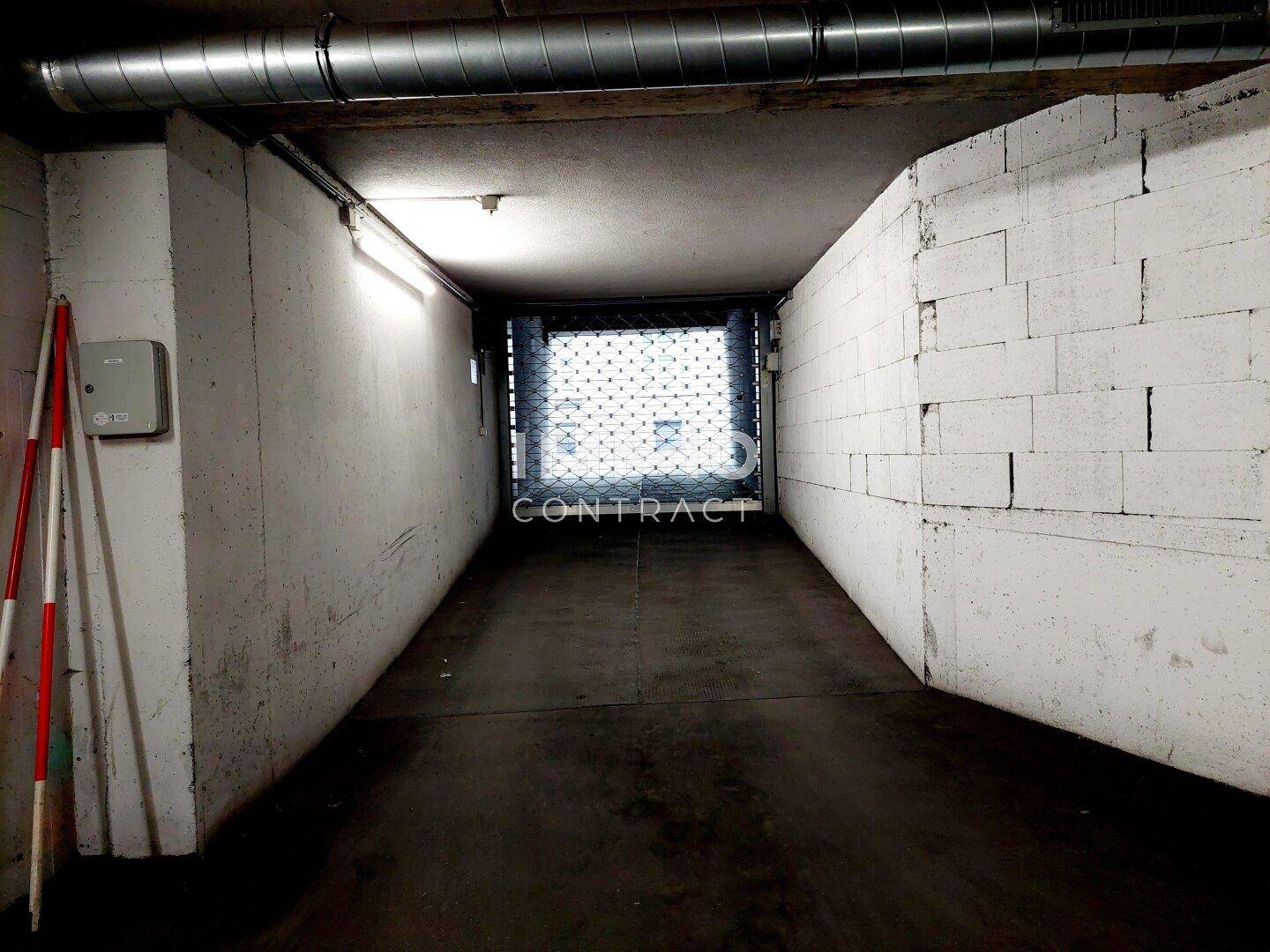 Einfahrt zu einer Tiefgarage mit Betonwänden und sichtbaren Lüftungsrohren.