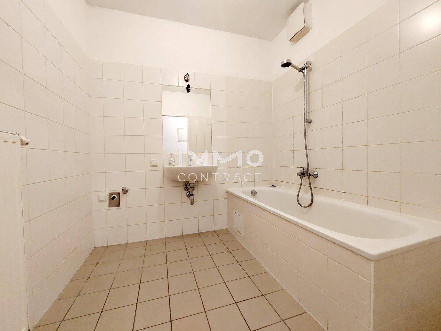 Badezimmer mit weißen Fliesen, Badewanne mit Duschfunktion und Einzelwaschbecken.