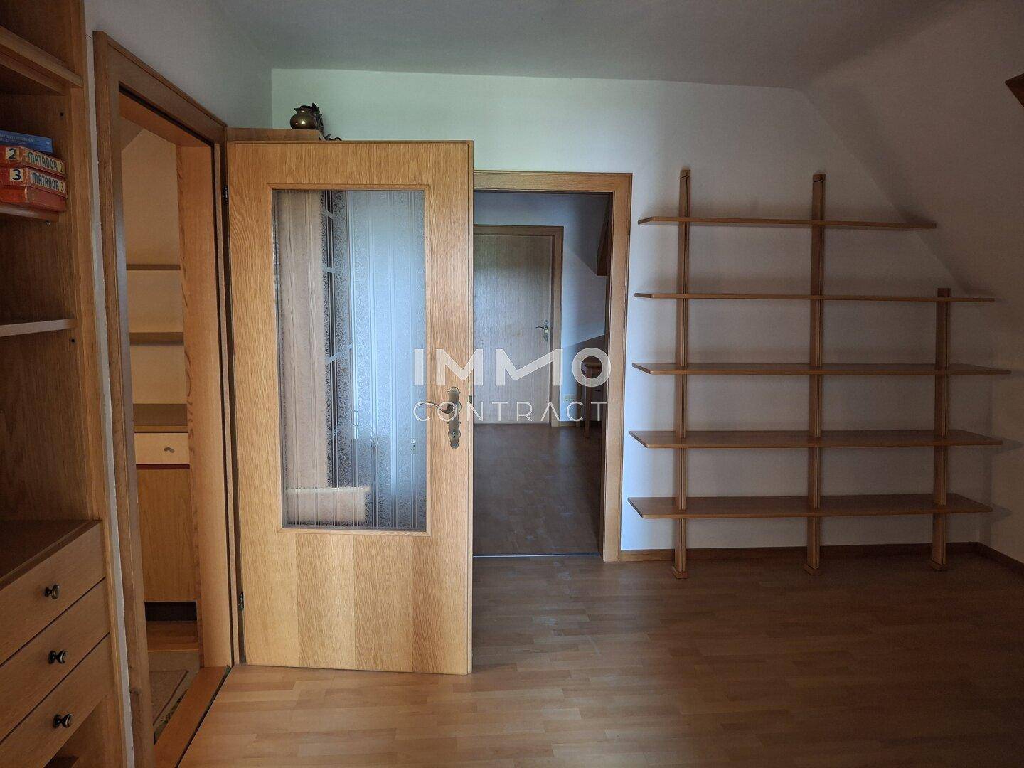 Dachzimmer mit Regalen, Laminatboden und Zugang zu einem weiteren Raum.