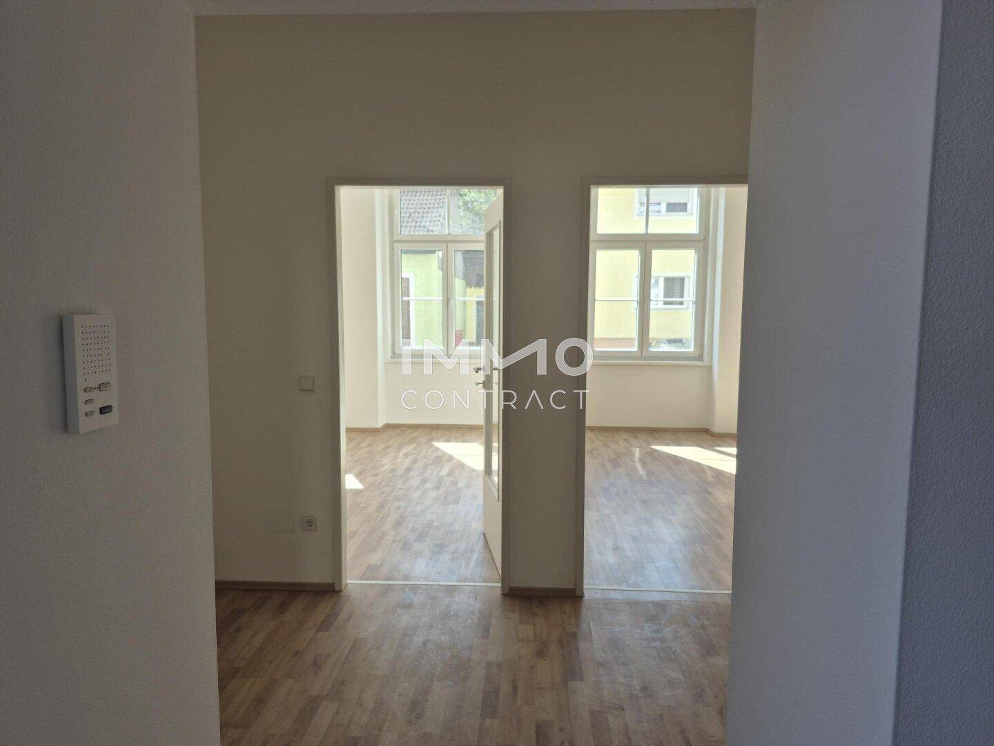 Heller Flur mit Blick in zwei angrenzende, leere Zimmer mit Laminatboden und großen Fenstern.