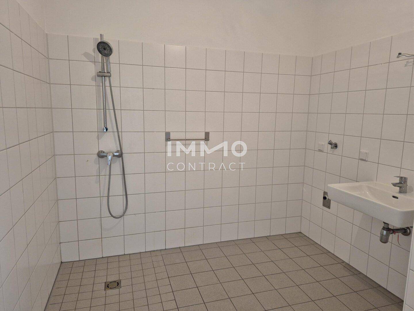 Funktionales Badezimmer mit weißen Fliesen, einer Dusche und einem Waschbecken.