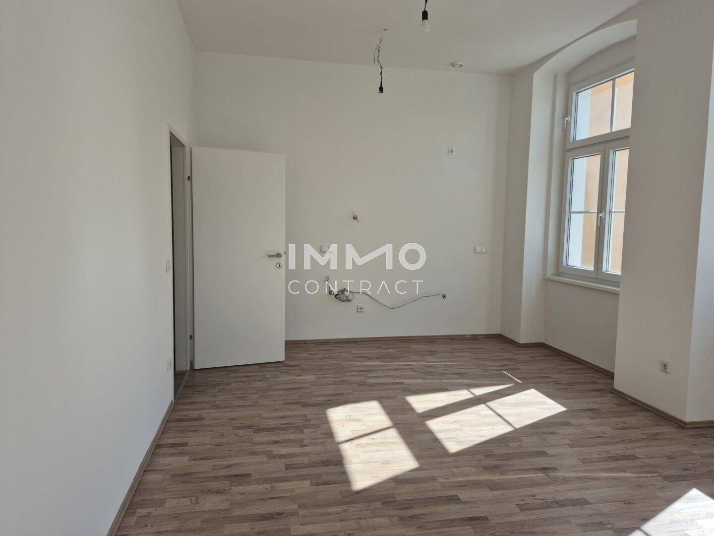 Geräumiges Zimmer mit Laminatboden und Fenster, das auf die Straße blickt.
