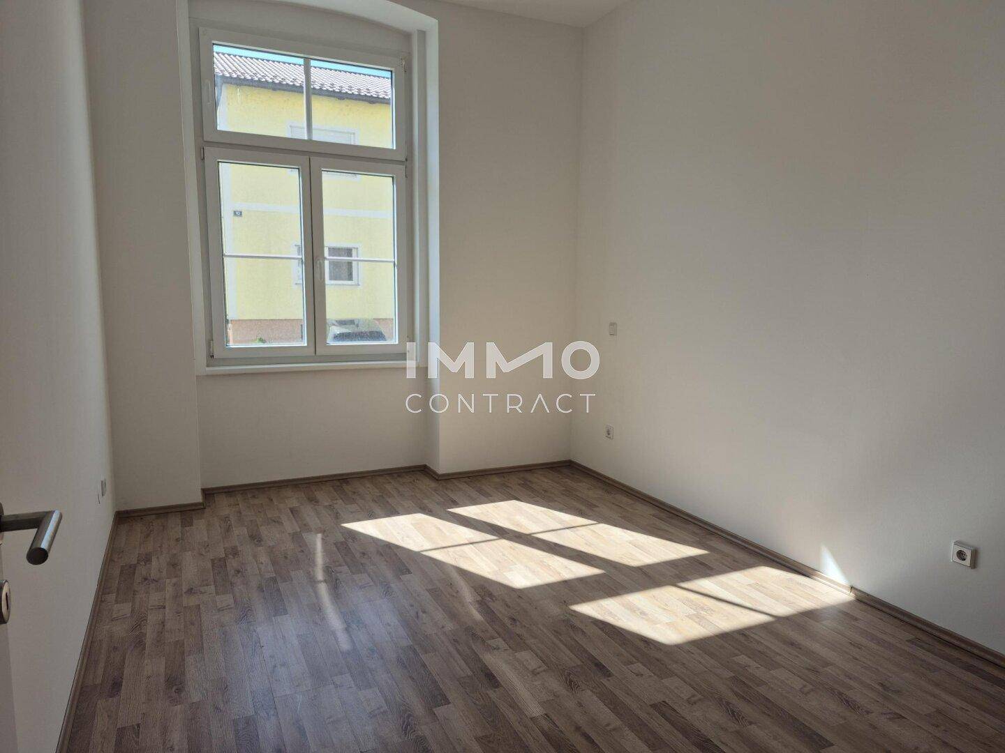 Sonniger Raum mit Laminatboden und großem Fenster, das viel natürliches Licht spendet.