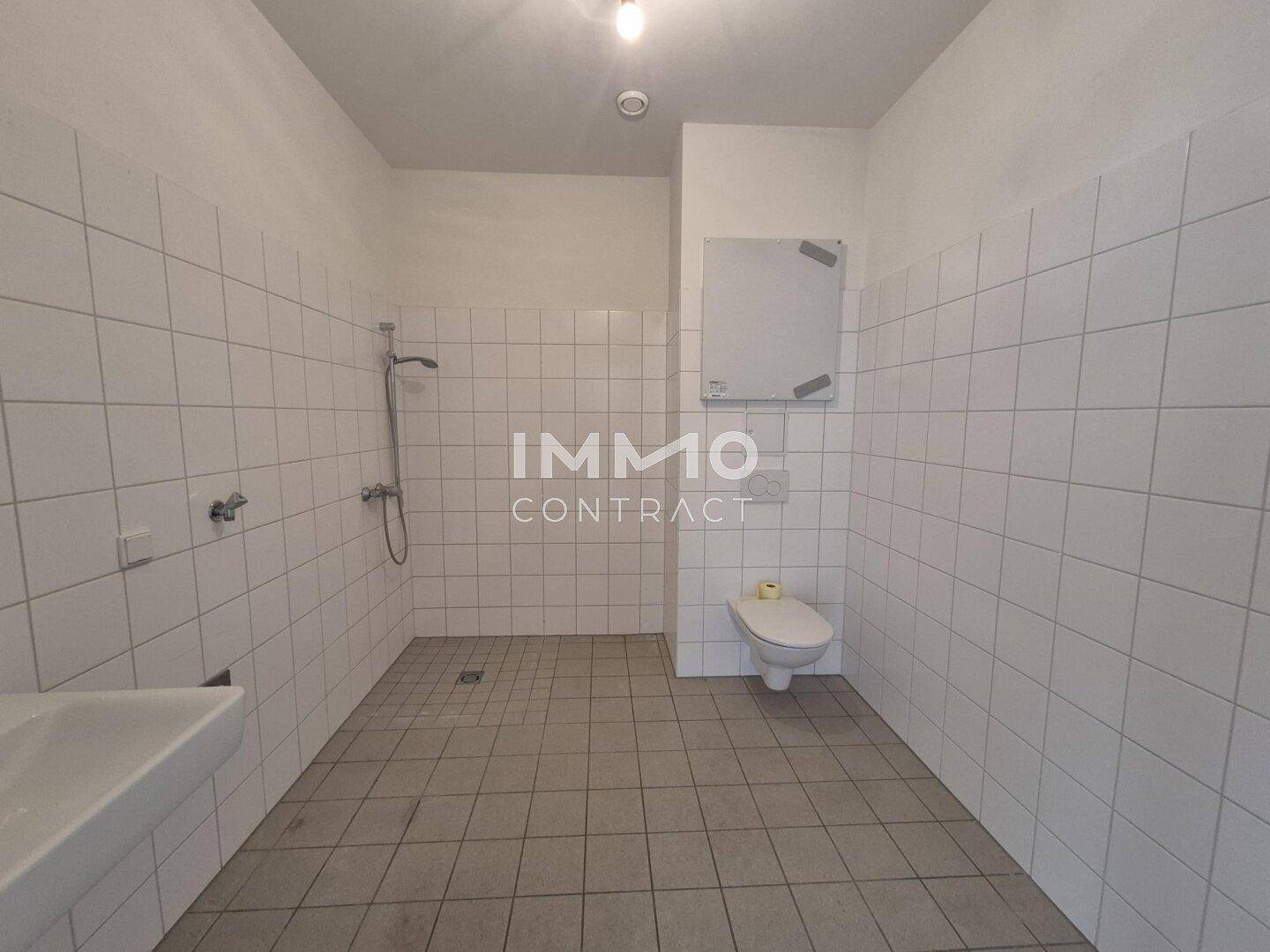 Funktionales Badezimmer mit weißen Fliesen, ebenerdiger Dusche und Toilette.