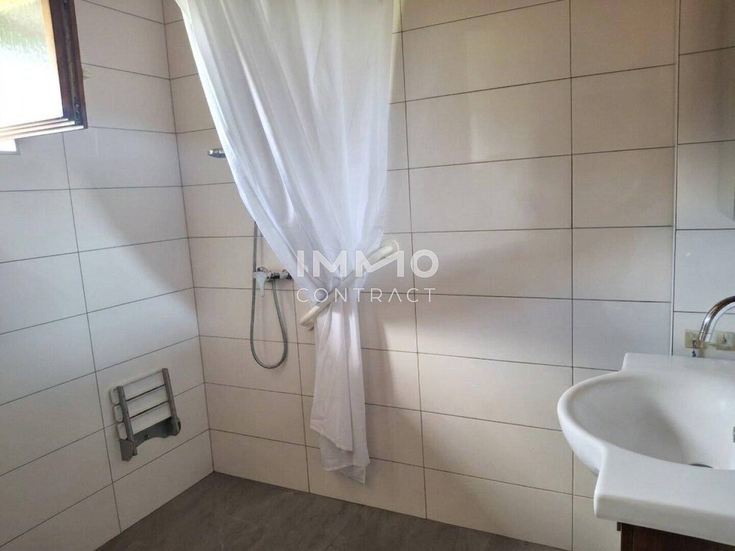 Badezimmer mit Duschbereich, Waschbecken und weißen Wandfliesen.