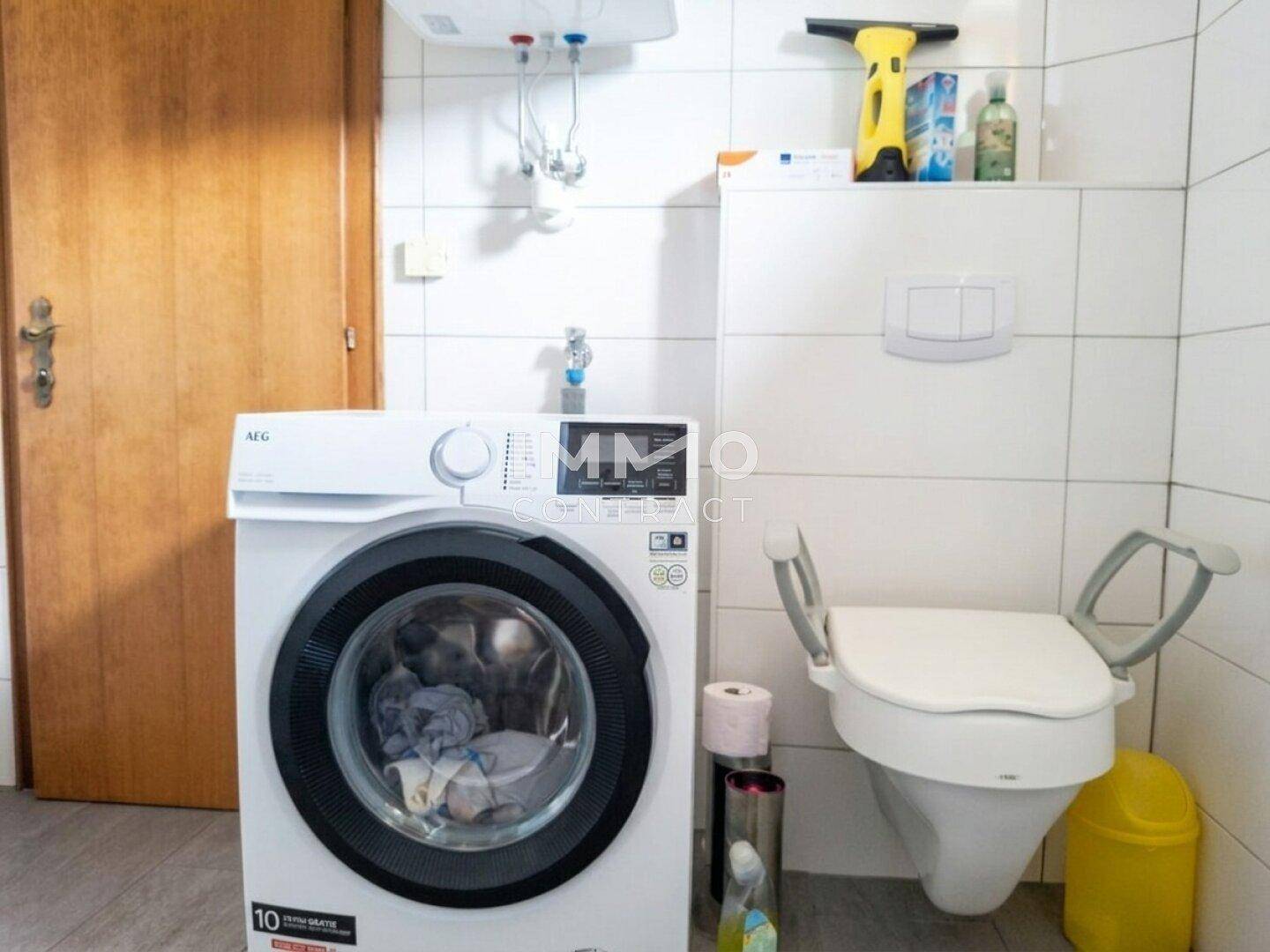 Badezimmer mit Waschmaschine, WC mit Haltegriffen und weißen Fliesen.