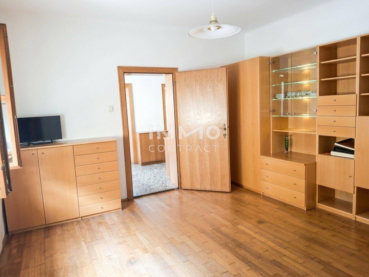 Helles Wohnzimmer mit Holzregalen, Parkettboden und Zugang zu einem weiteren Raum.