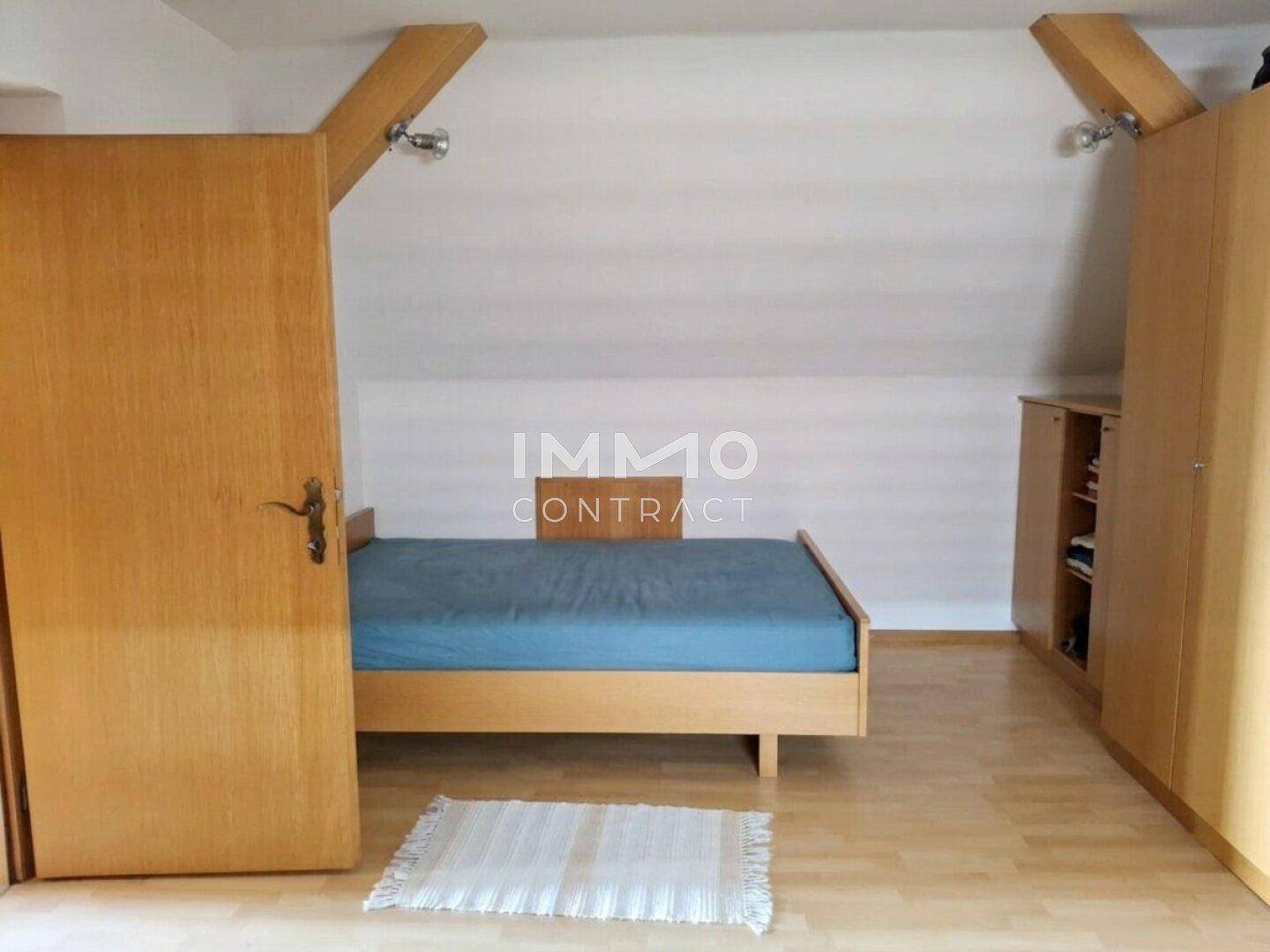 Dachzimmer mit Holzbett, Laminatboden und sichtbaren Dachbalken.