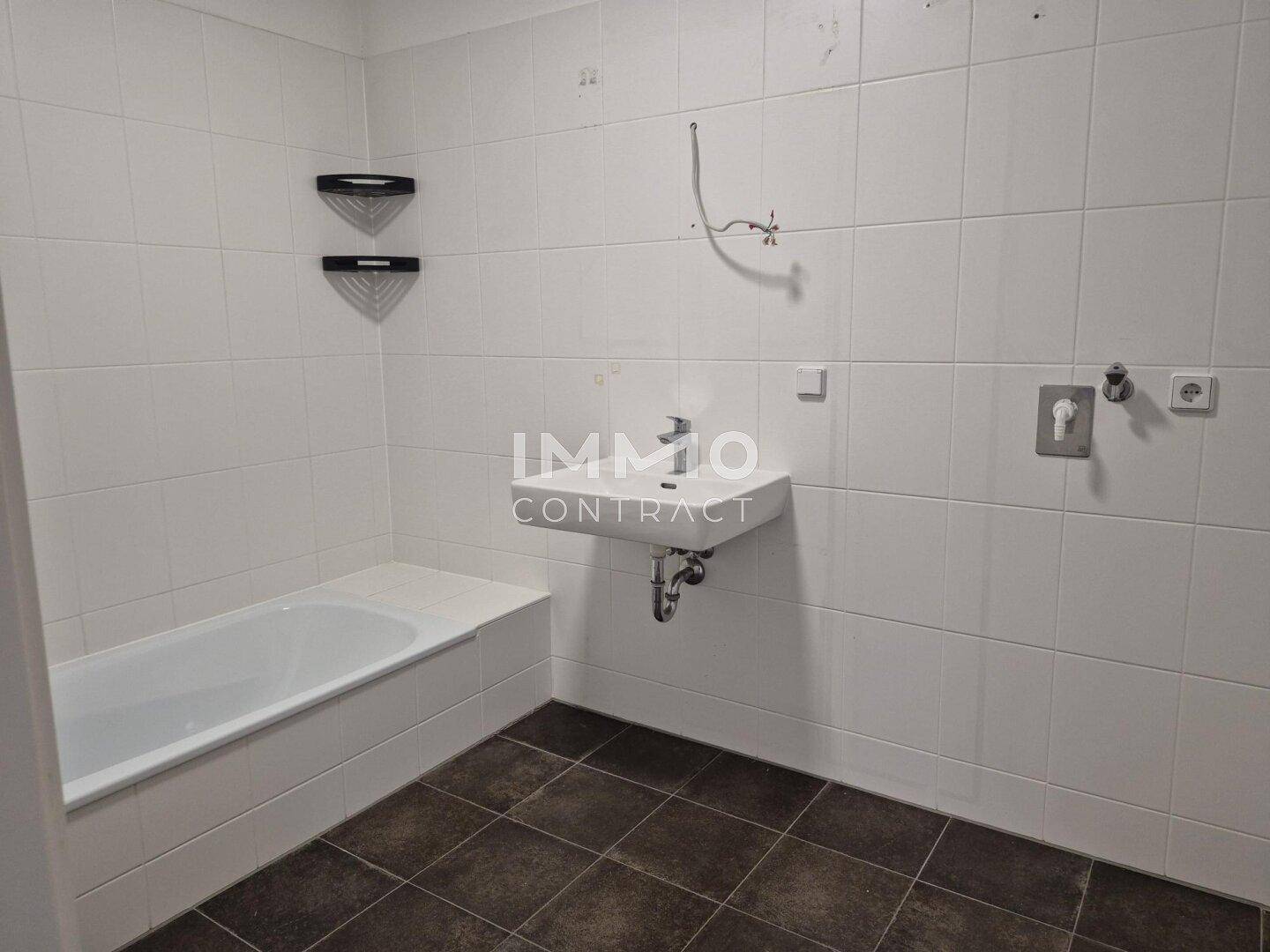 Badezimmer mit weißen Wandfliesen, dunklem Boden und einer Badewanne.
