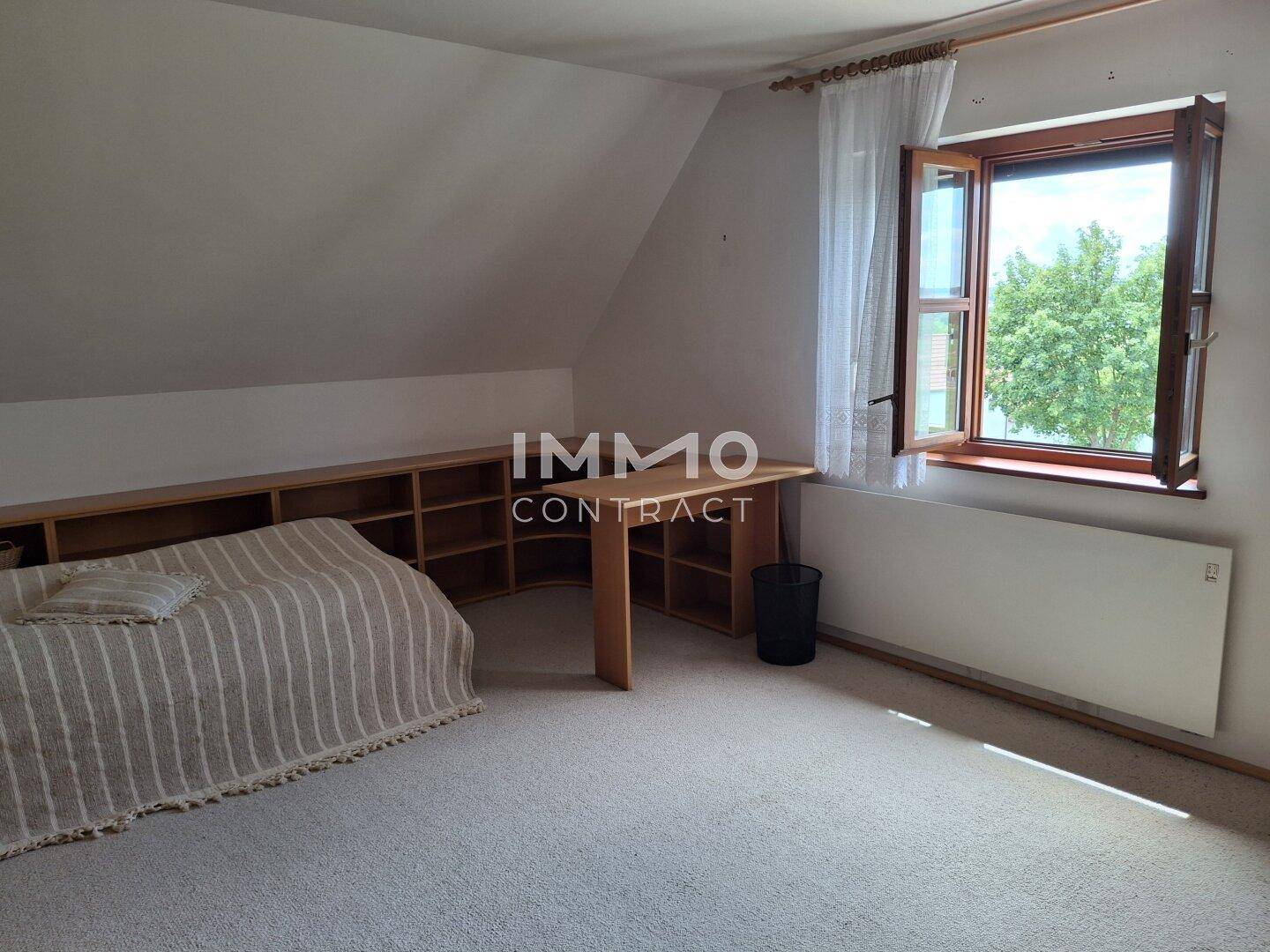Dachzimmer mit Bett, Schreibtisch, Teppichboden und Fenster mit Ausblick.