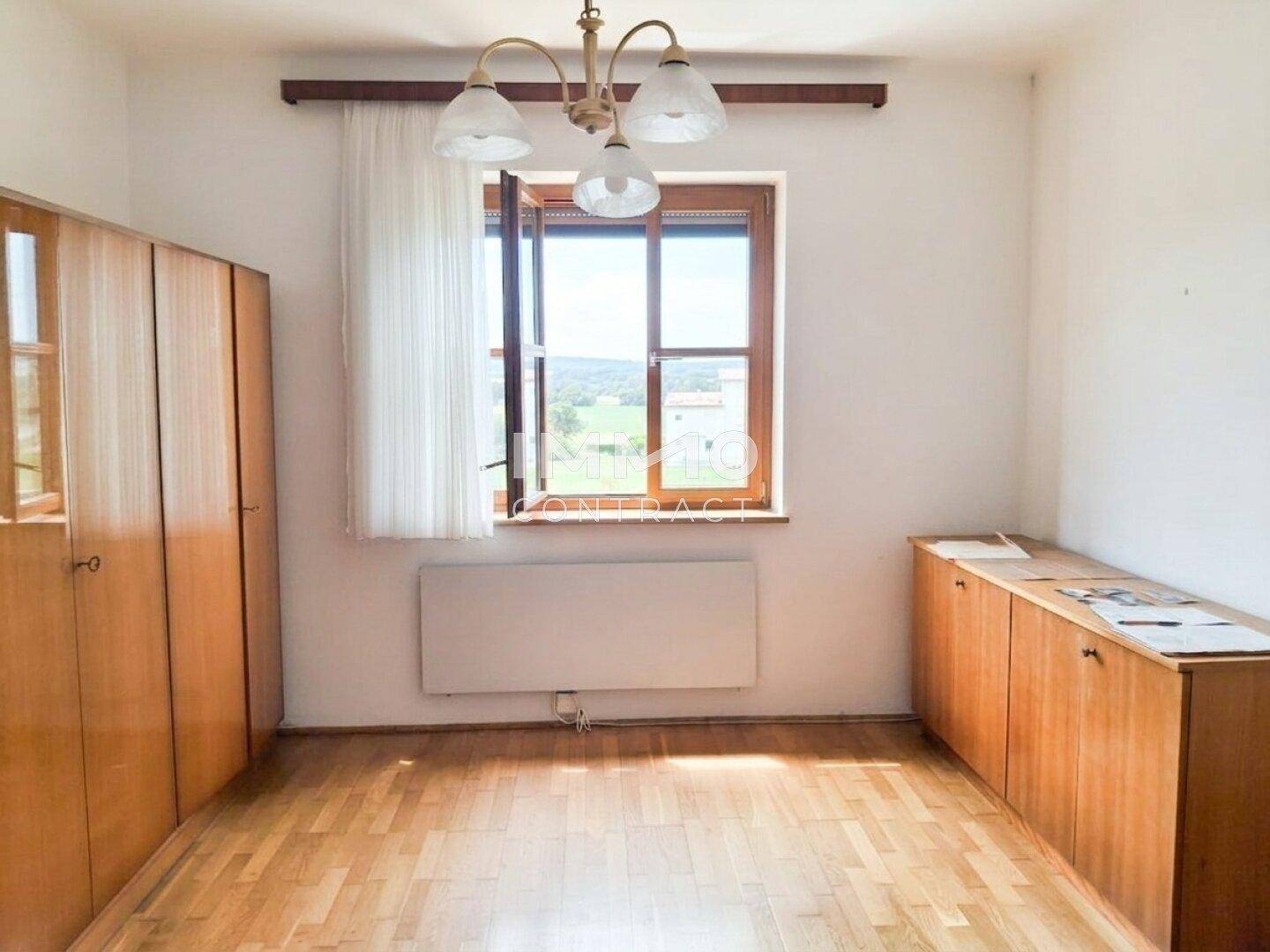 Helles Zimmer mit Holzschränken, Parkettboden und Fenster mit Blick ins Grüne.