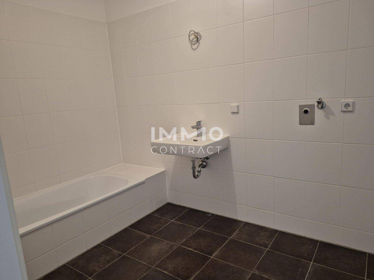 Modernes Badezimmer mit Badewanne, Waschbecken und dunklen Bodenfliesen.