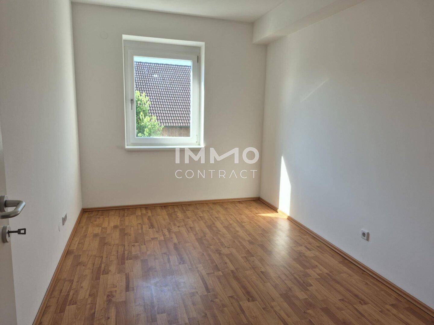Freundliches, leeres Zimmer mit Laminatboden und Fenster, ideal als Kinder- oder Gästezimmer.