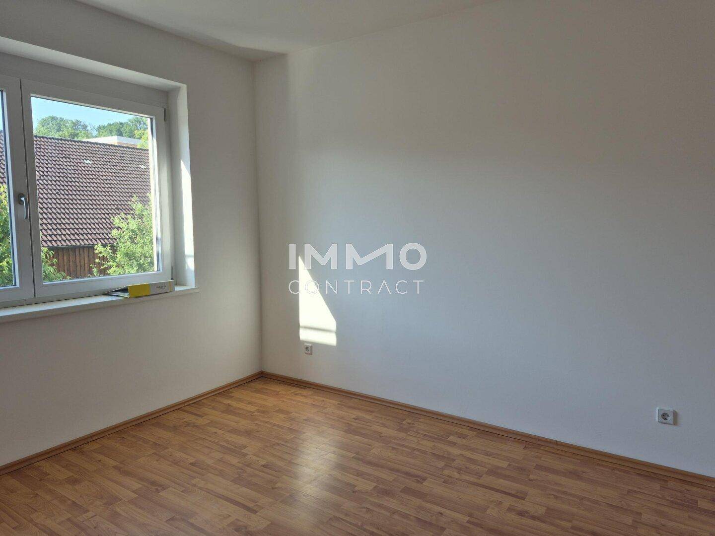 Helles Schlafzimmer mit Laminatboden und Blick ins Grüne durch das große Fenster.