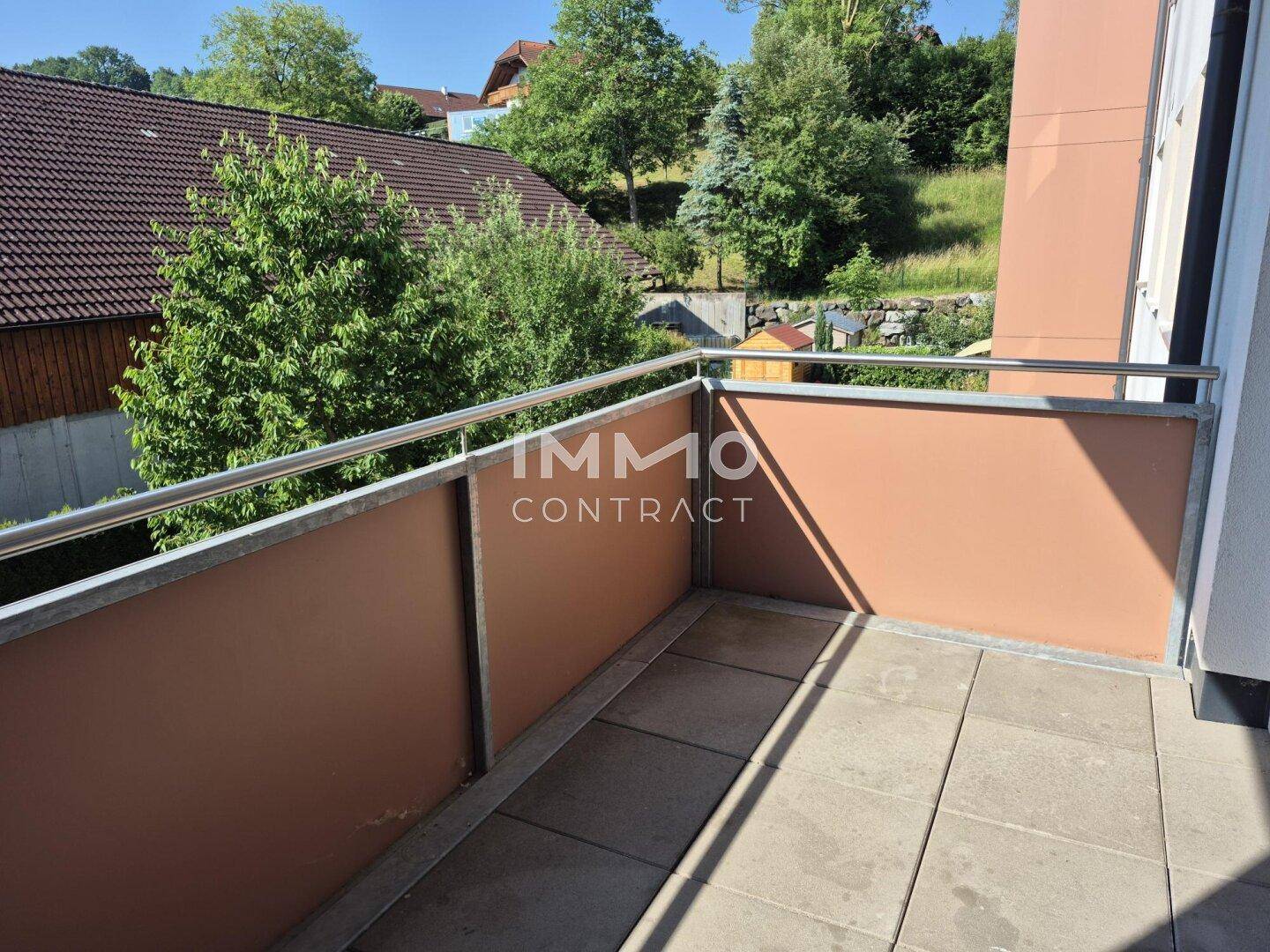 Sonniger Balkon mit Fliesenboden und Geländer, bietet einen angenehmen Blick ins Grüne.