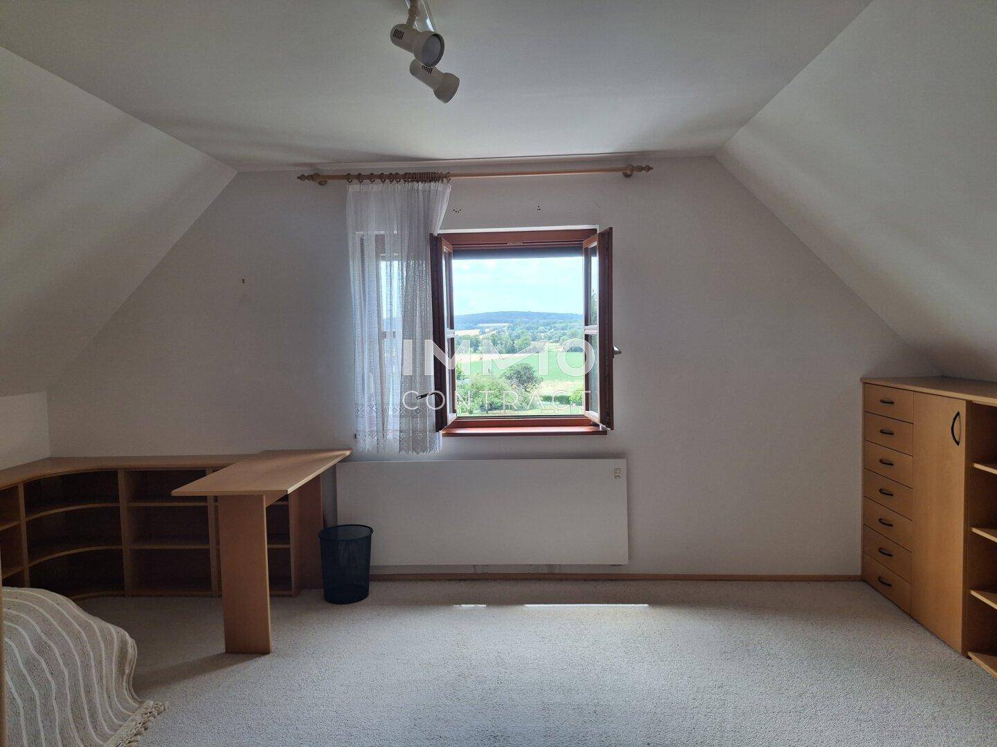 Helles Dachzimmer mit Teppichboden, Schreibtisch und Fenster mit weitem Blick.