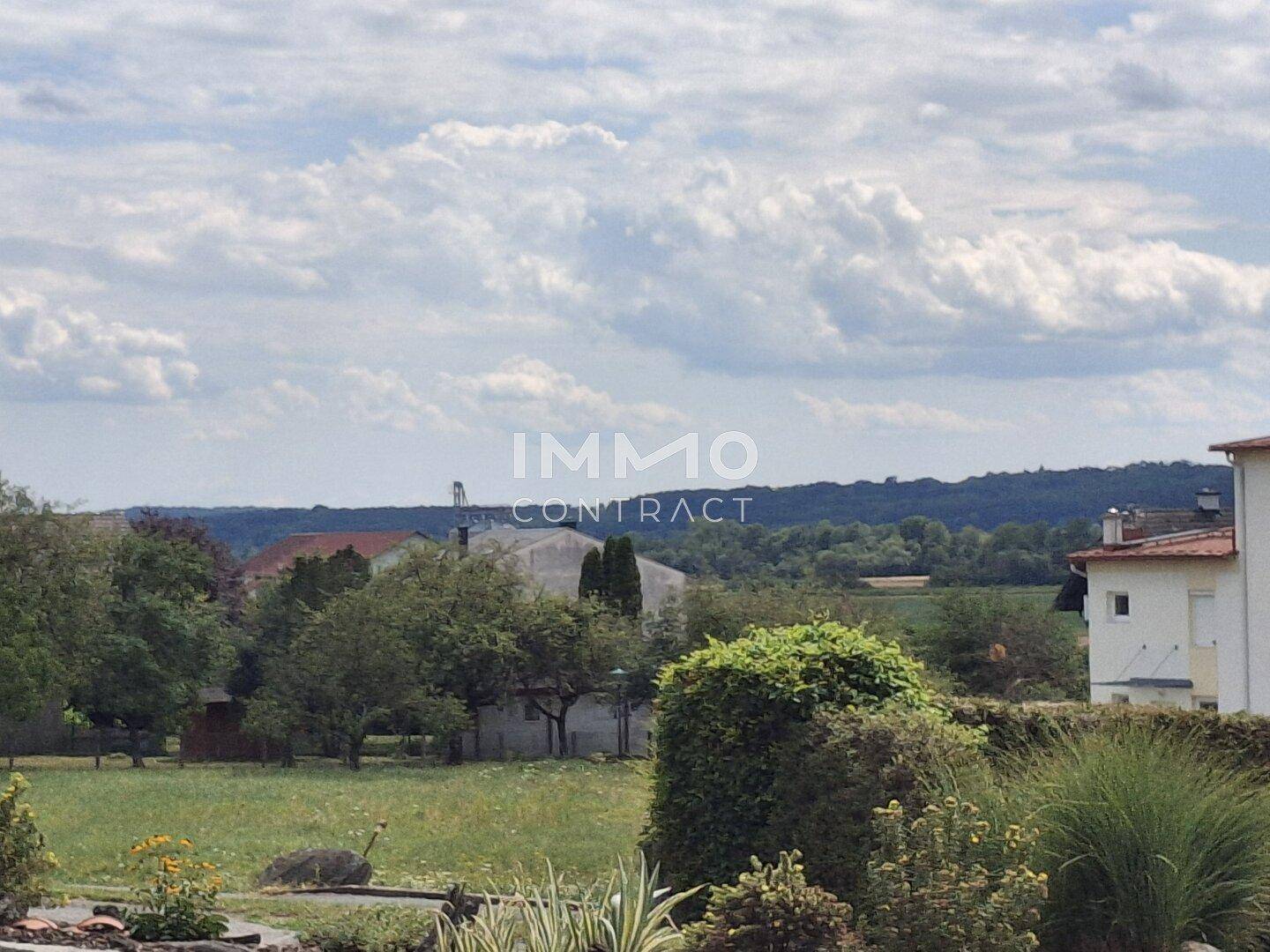 Weitläufiger Blick über grüne Landschaft und Dächer von Häusern.