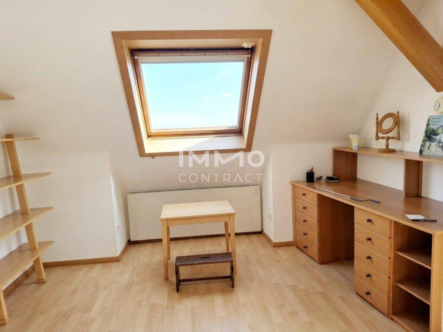 Dachzimmer als Büro eingerichtet mit Schreibtisch, Regalen und Dachfenster.