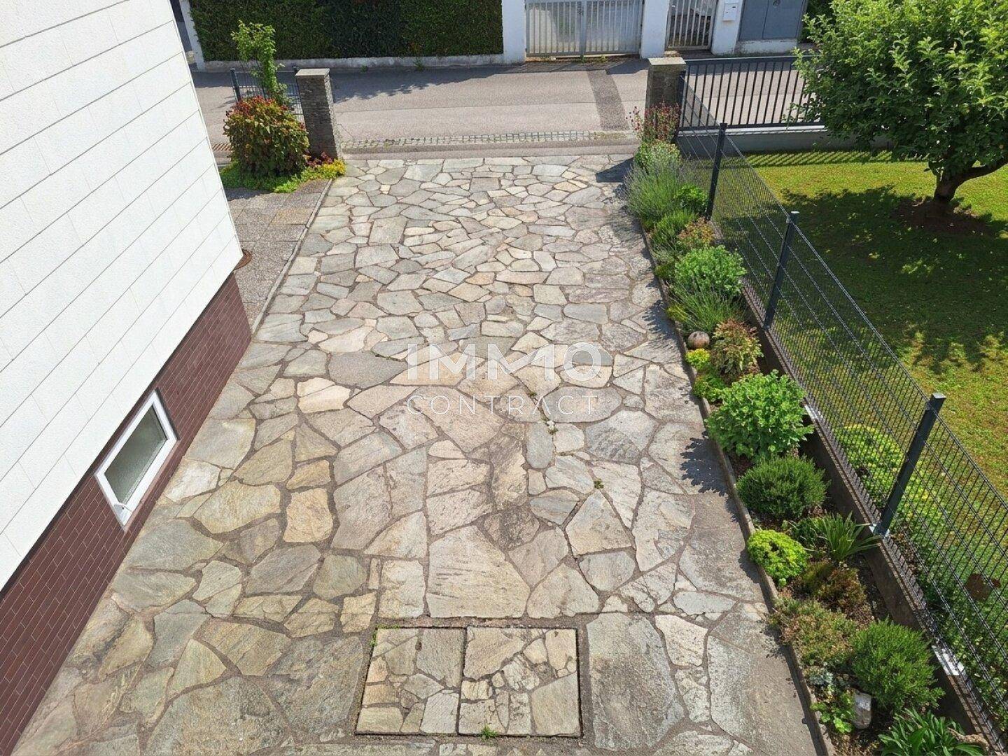 Zufahrt zum Grundstück mit unregelmäßigen Steinplatten und gepflegten Beeten an den Seiten.