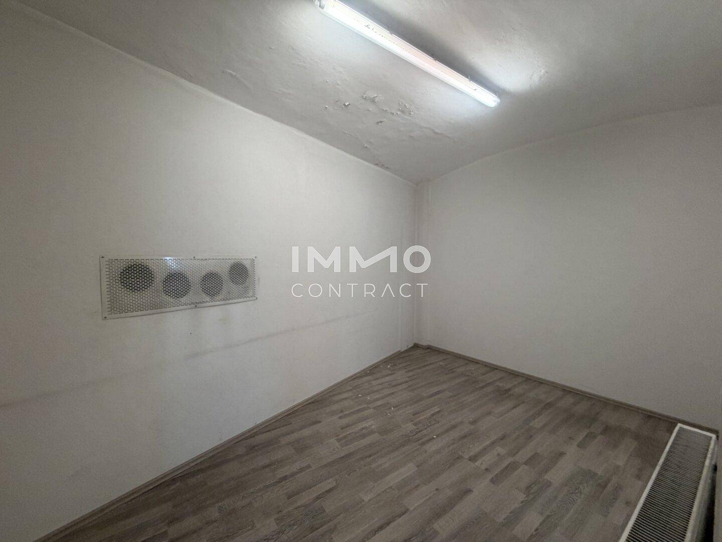 Kleiner, leerer Raum mit Laminatboden, weißen Wänden und einer Lüftungseinheit an der Wand.