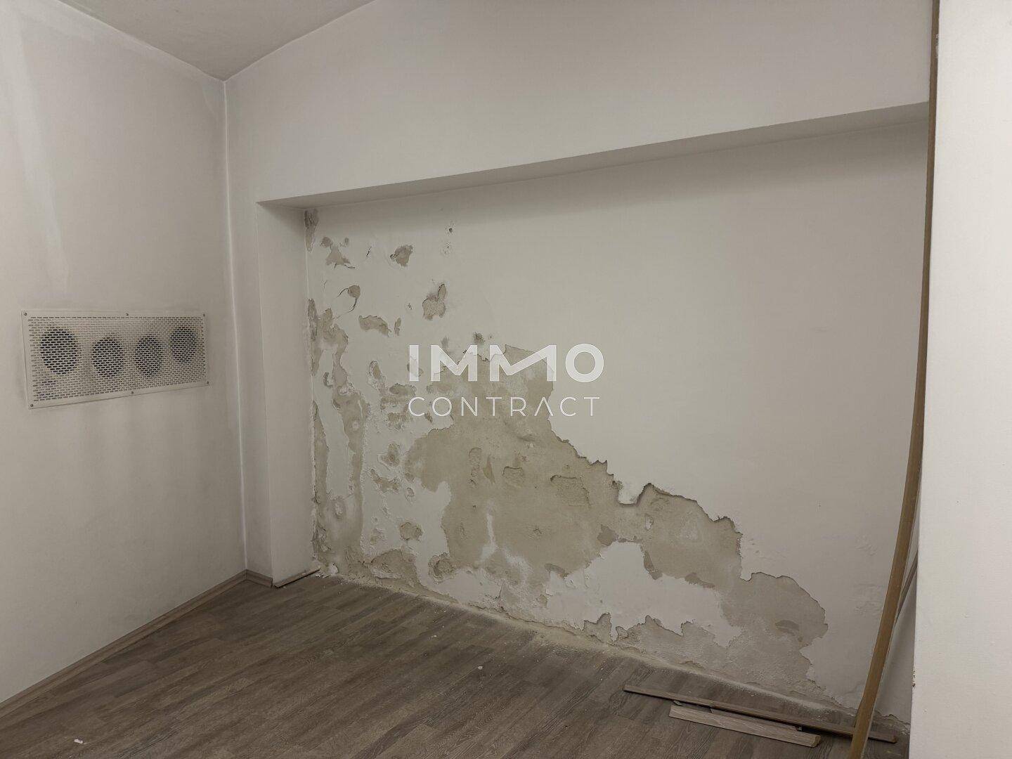 Nahaufnahme einer Wand mit stark abblätternder Farbe in einem leeren Raum mit Laminatboden.