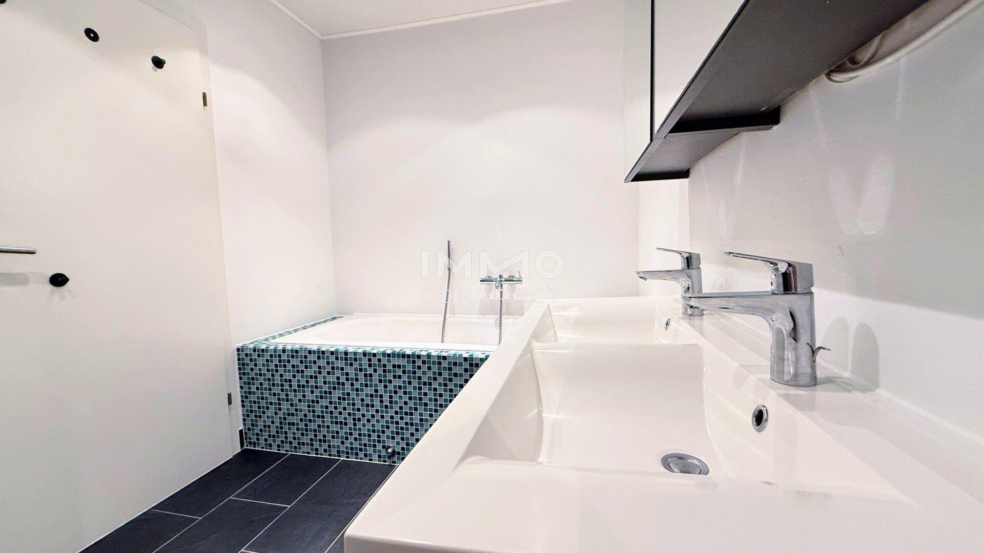Modernes Badezimmer mit Badewanne, Einzelwaschbecken und dunklen Bodenfliesen.