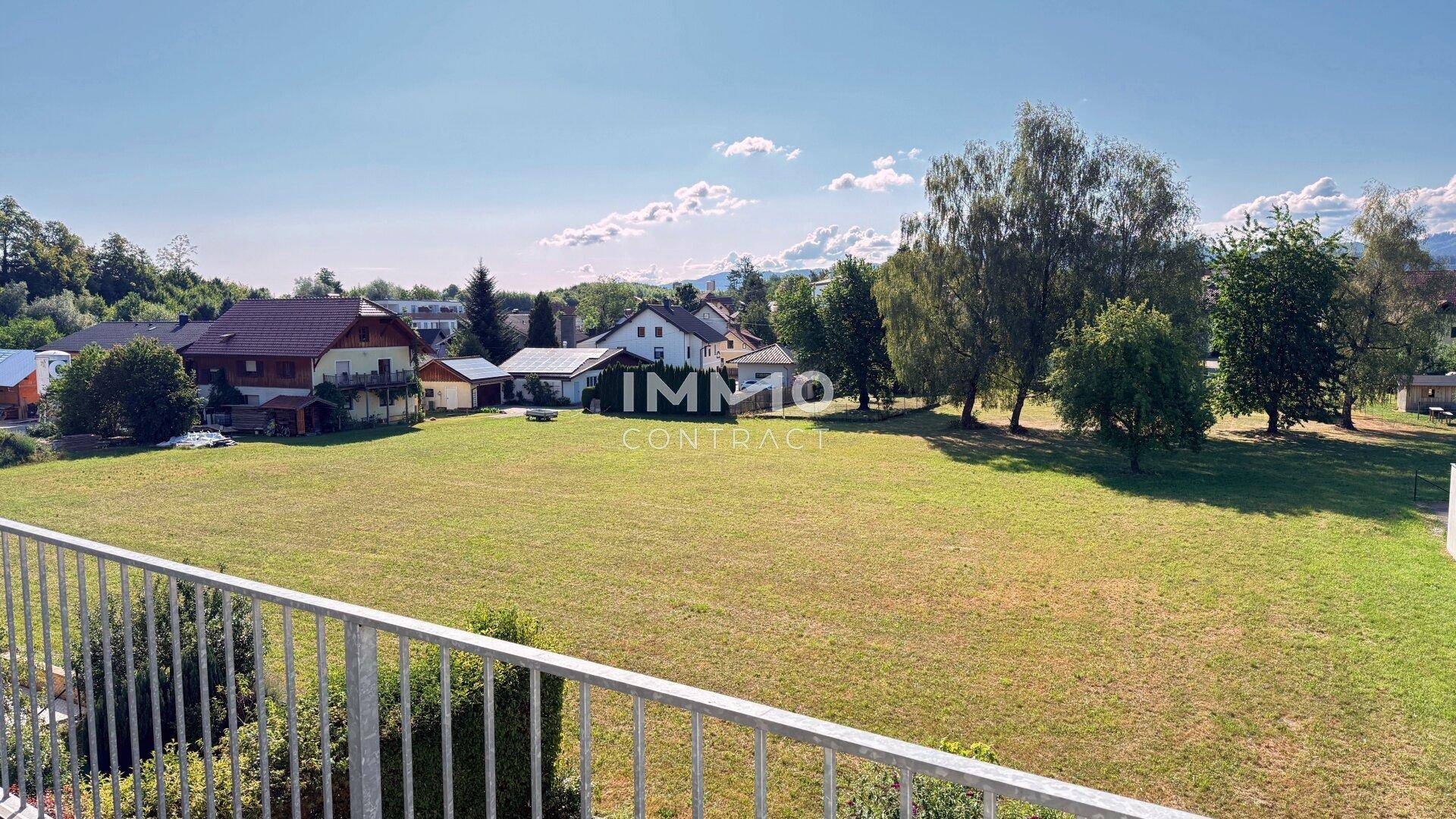 Weitläufiger Ausblick von einem Balkon auf grüne Felder, Bäume und die umliegende Landschaft.