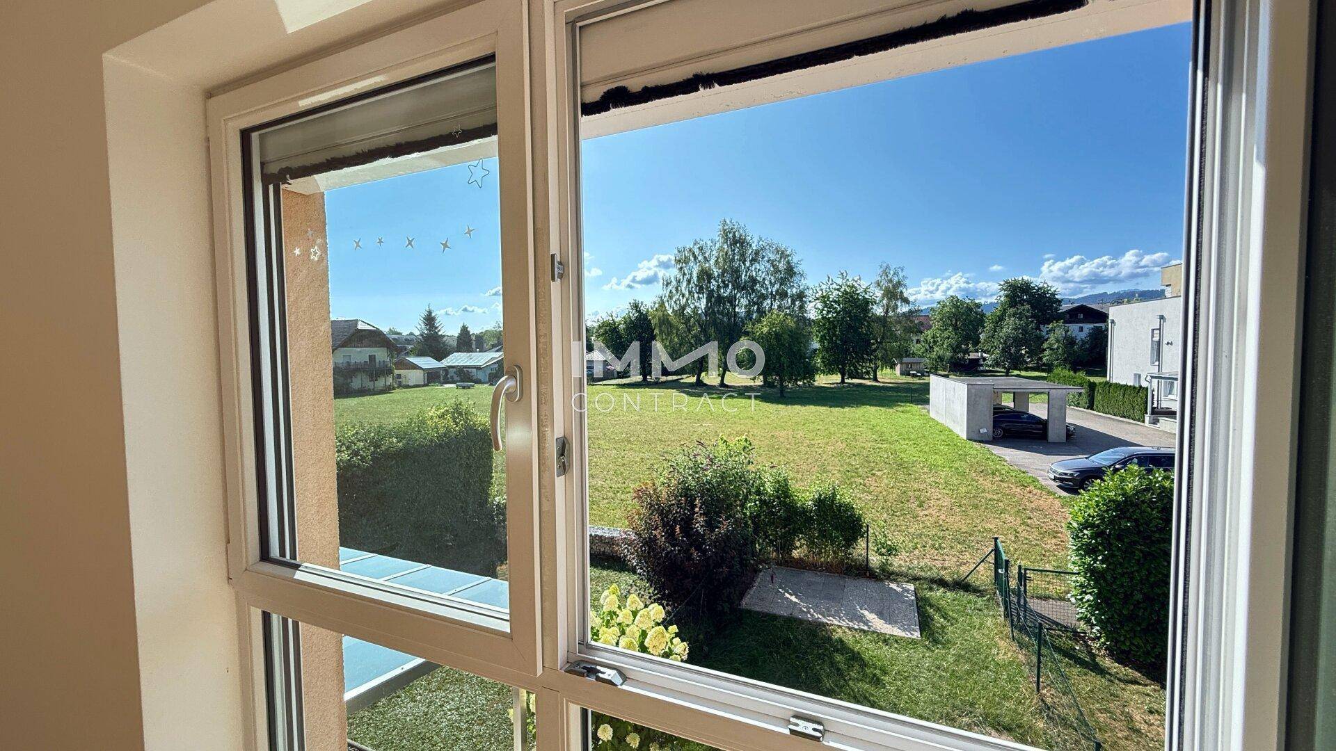 Weitläufiger Blick aus dem Fenster auf eine grüne Landschaft mit Bäumen und Häusern.