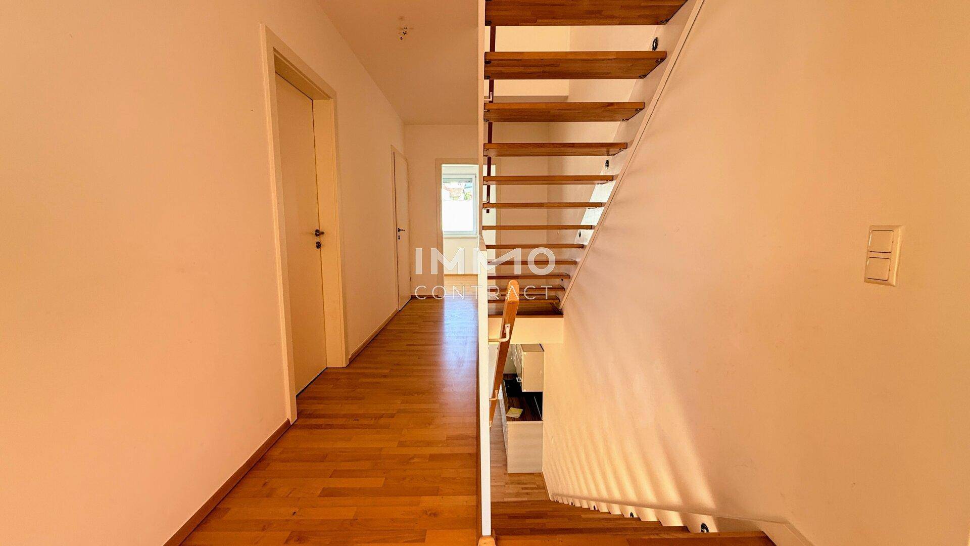 Heller Flur mit Holzfußboden und einer offenen Holztreppe zum Obergeschoss.