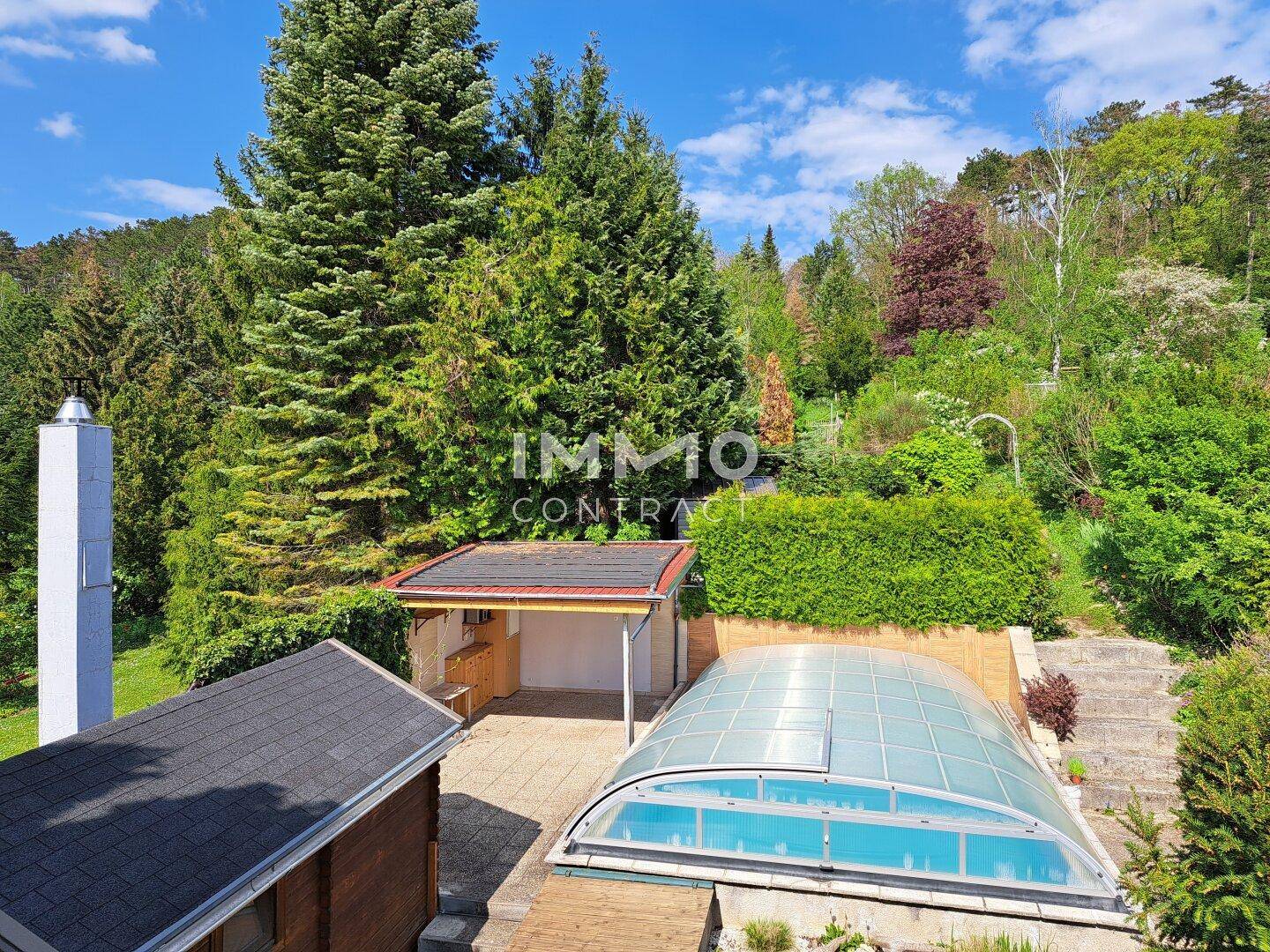 Großer Gartenbereich mit überdachtem Pool, Terrasse und üppiger Vegetation im Hintergrund.