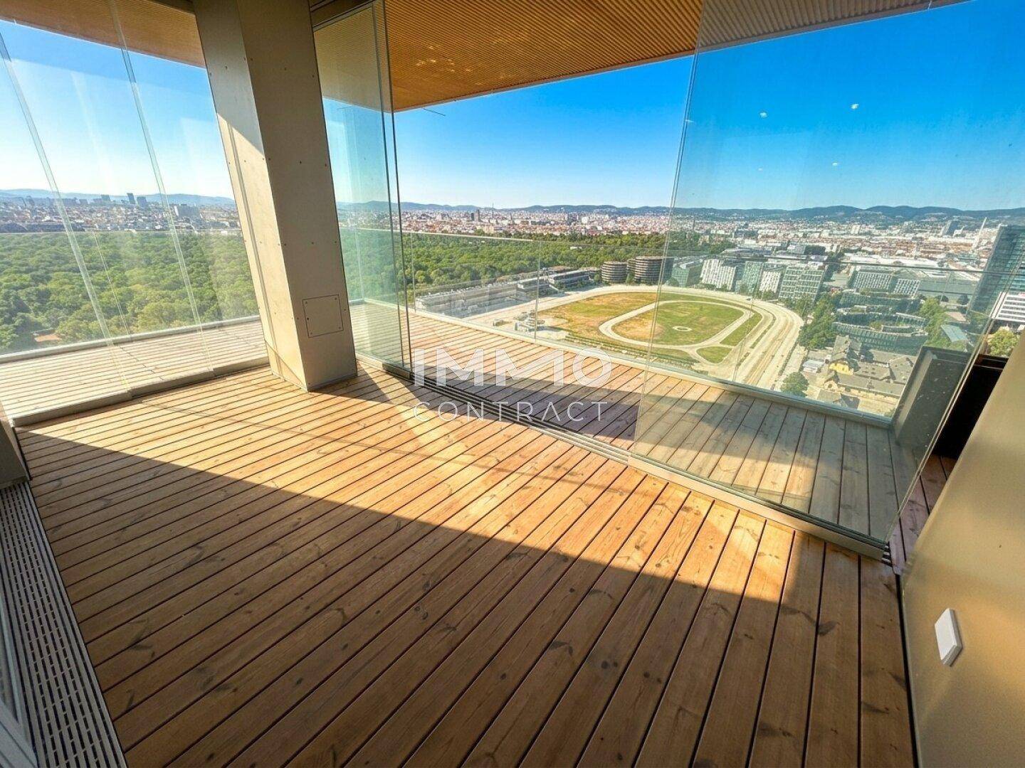 Geräumiger Balkon mit Holzboden und weitem Blick über die Stadt und Grünflächen.