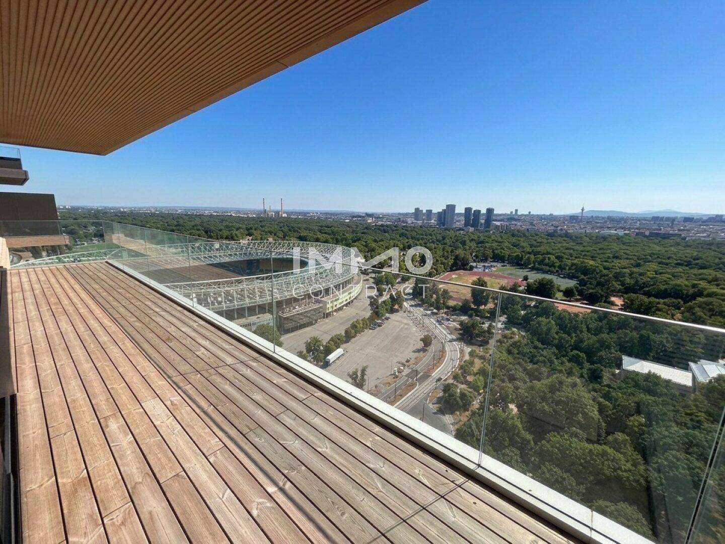 Große Dachterrasse mit Holzboden, Glasgeländer und weitem Blick auf die Stadt und das Stadion.
