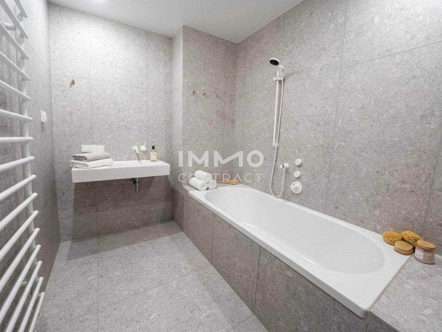 Helles Badezimmer mit Badewanne, schwebendem Waschbecken und grauen Fliesen.