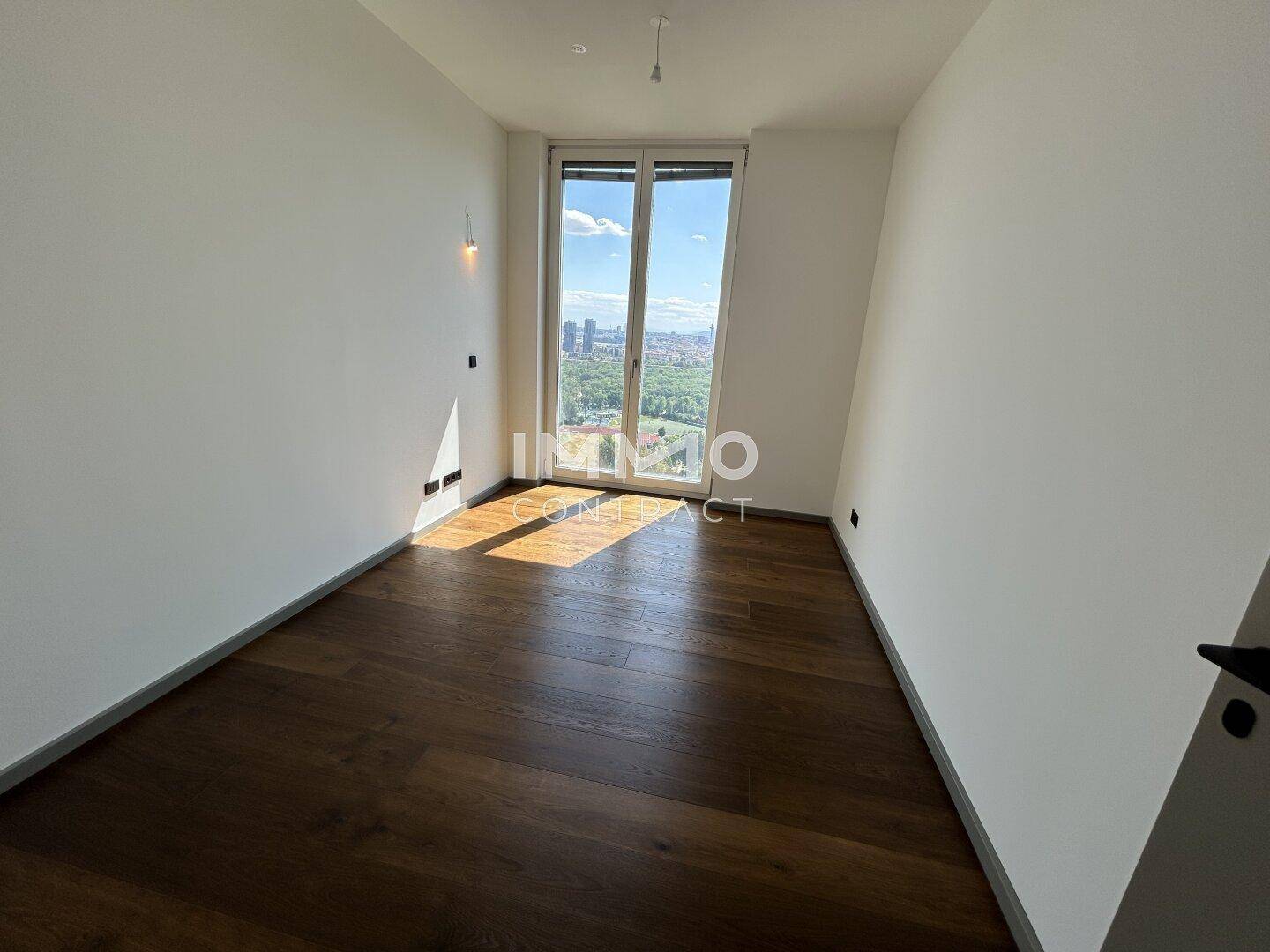 Leeres Zimmer mit Holzboden und bodentiefen Fenstern bietet viel Tageslicht und Ausblick.